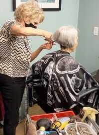 Photo of Kathleen Parker giving a resident a hair cut.